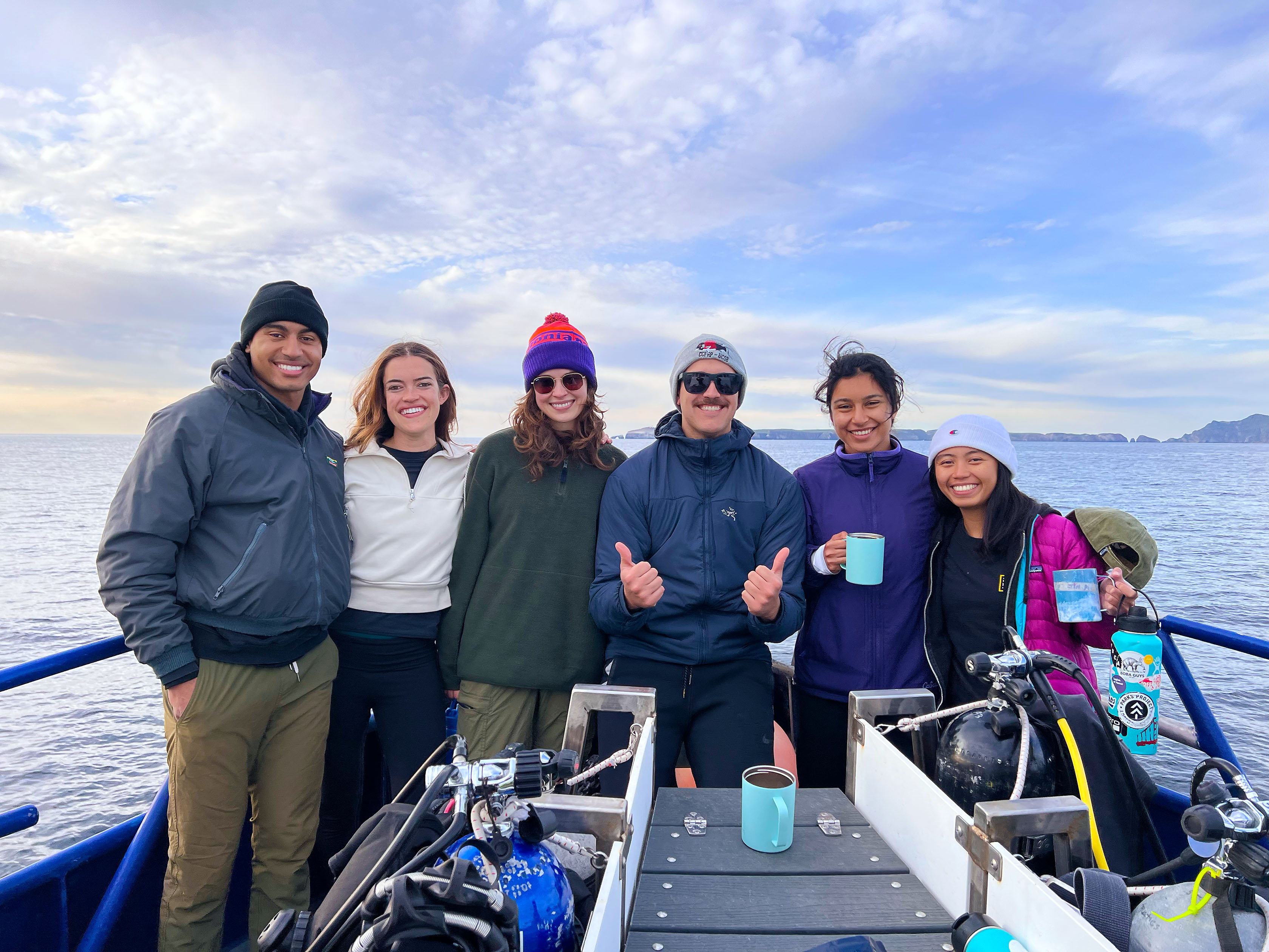 Group of 6 students in a boat, 4 girls, 2 boys, all smiling at the camera