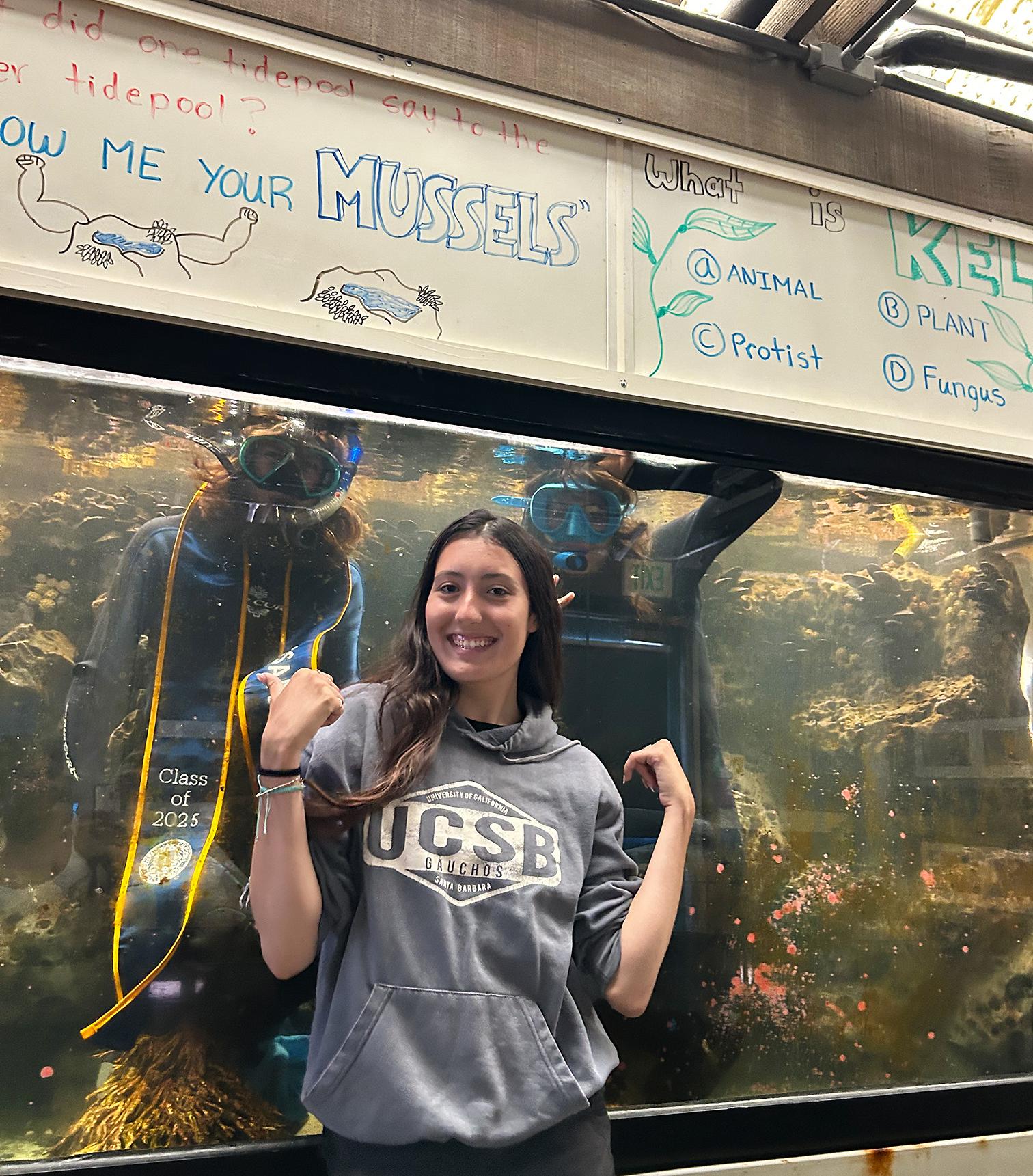 Sophia in front of tank with inside Marine (left), and Gainna (right) wearing their wetsuit, mask, and UCSB stole
