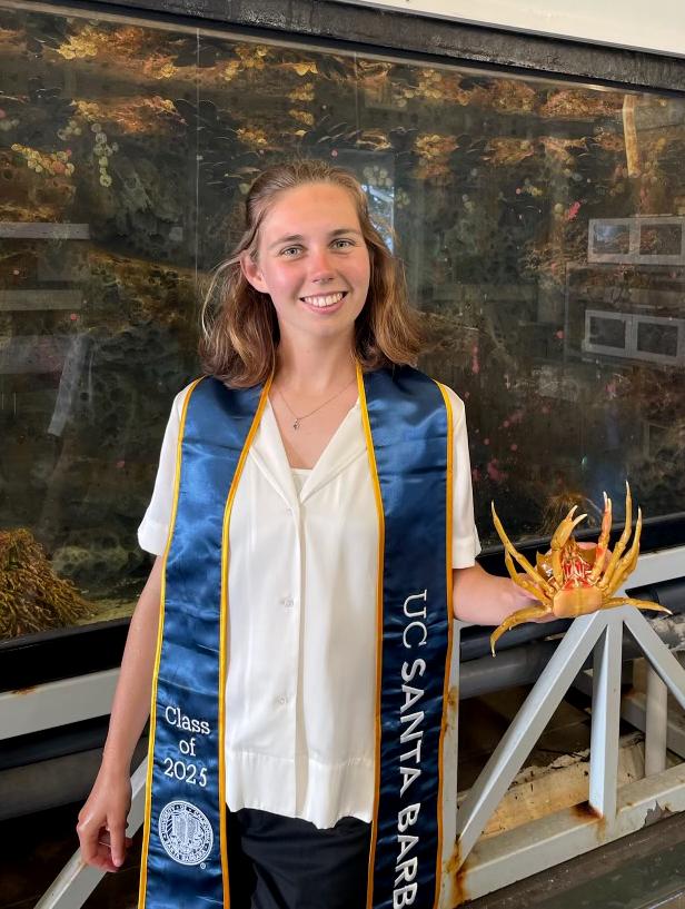 Marine holding a crab wearing with her UCSB graduation stole at The REEF