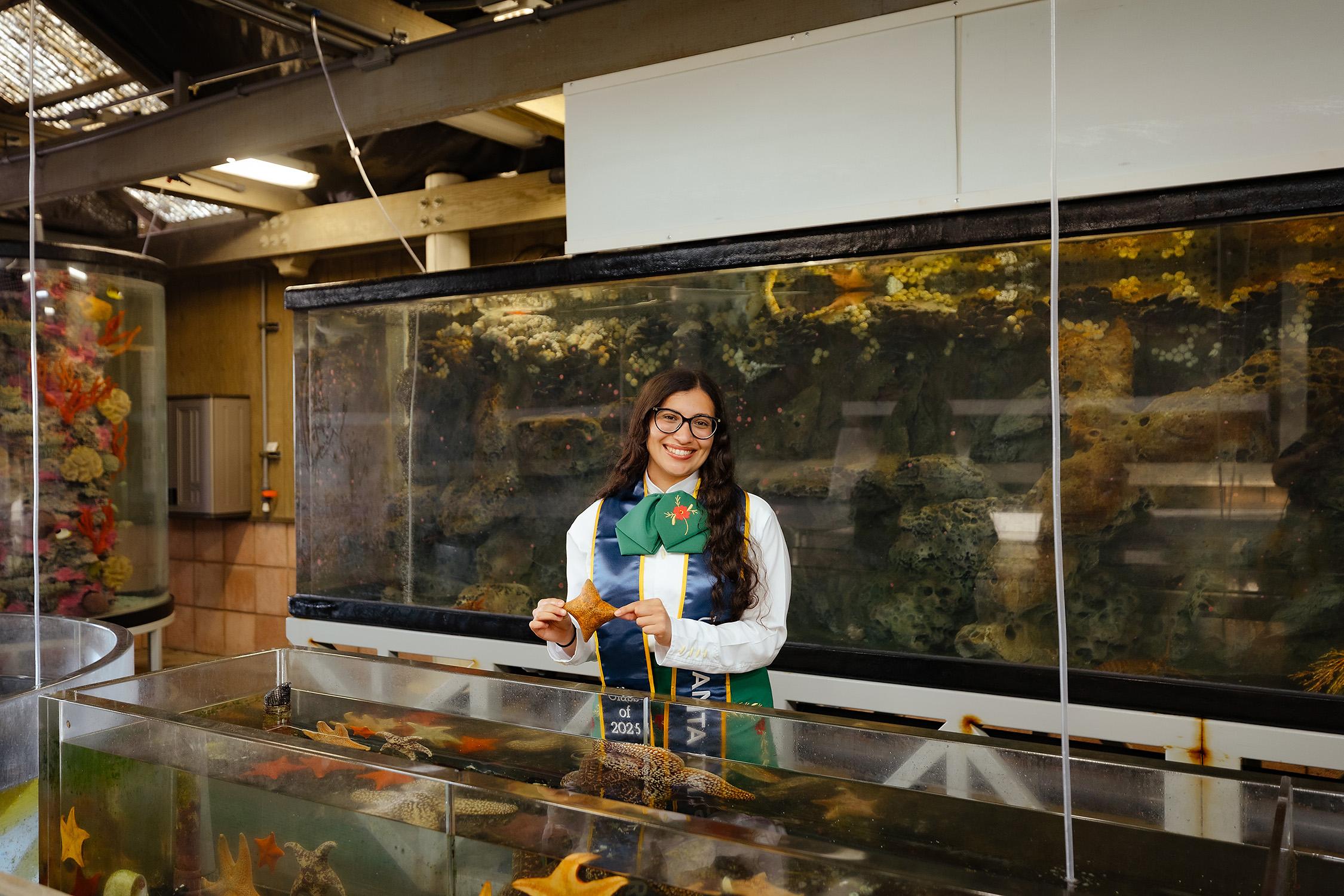 Sarah holding an orange sea star behind a touch tank