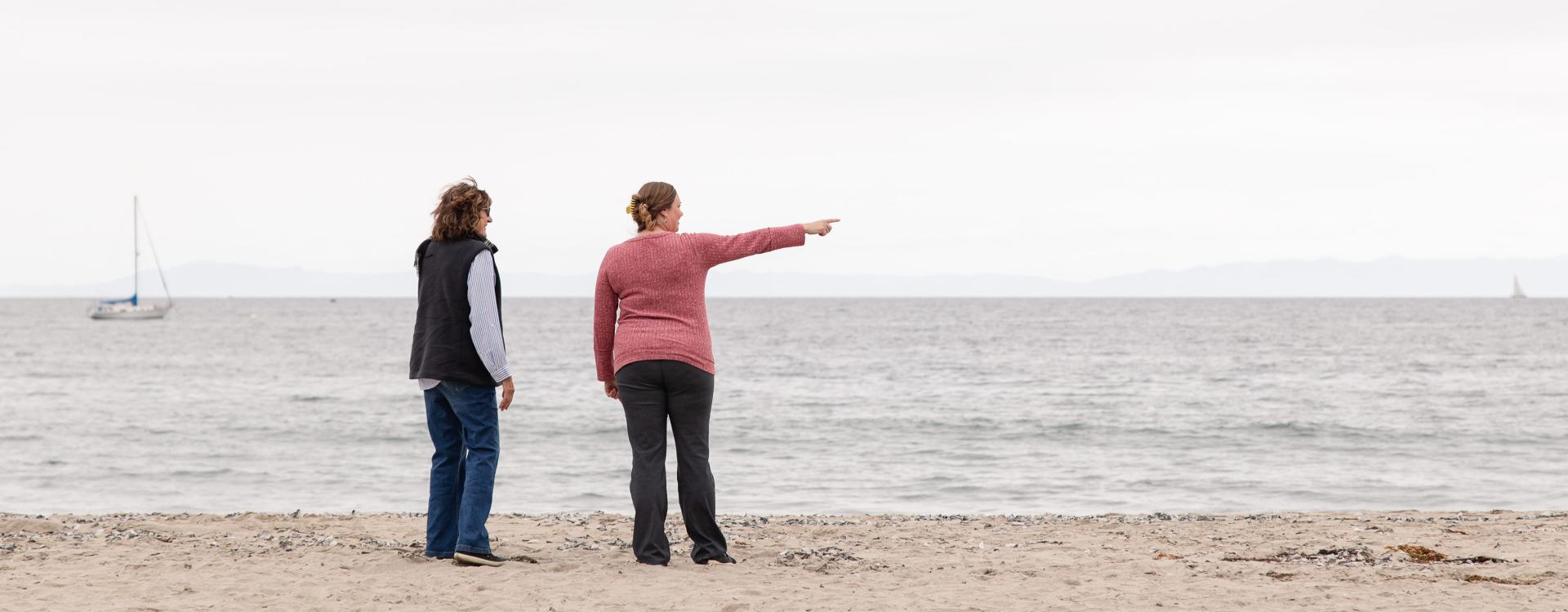 Hillary Hauser and Karina Johnston from the back standing on shore and looking at the ocean. Kanina on Hillary's right side is pointing at the sea