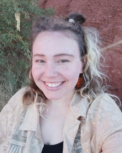 Siena smiling in front of red rocks and mesquite tree