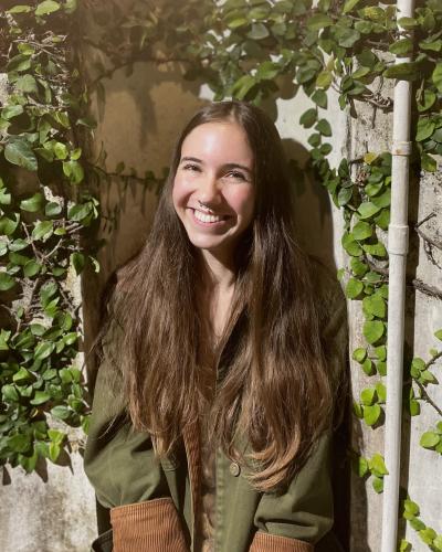 A young woman smiles in front of a wall covered in ivy 