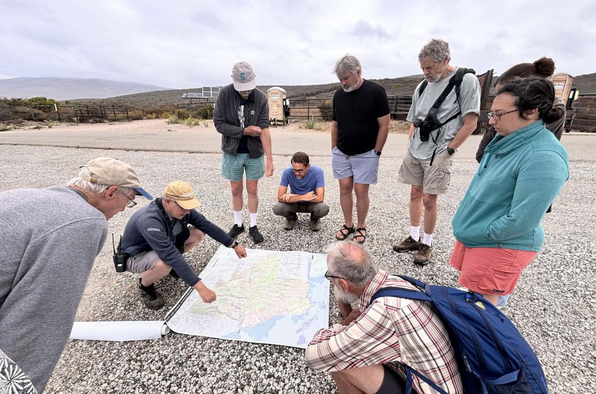 Group of eight scientist gathered around map on ground UCSB's Dangermond Preserve