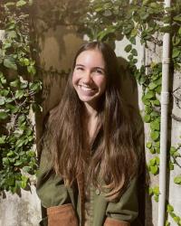 A young woman smiles in front of a wall covered in ivy 