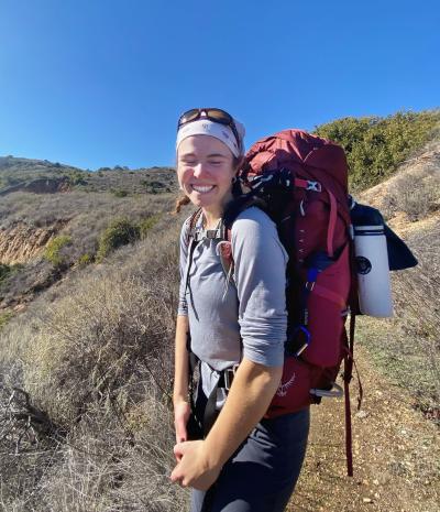 Francesca with backpack hiking in mountain trail, bluest sky