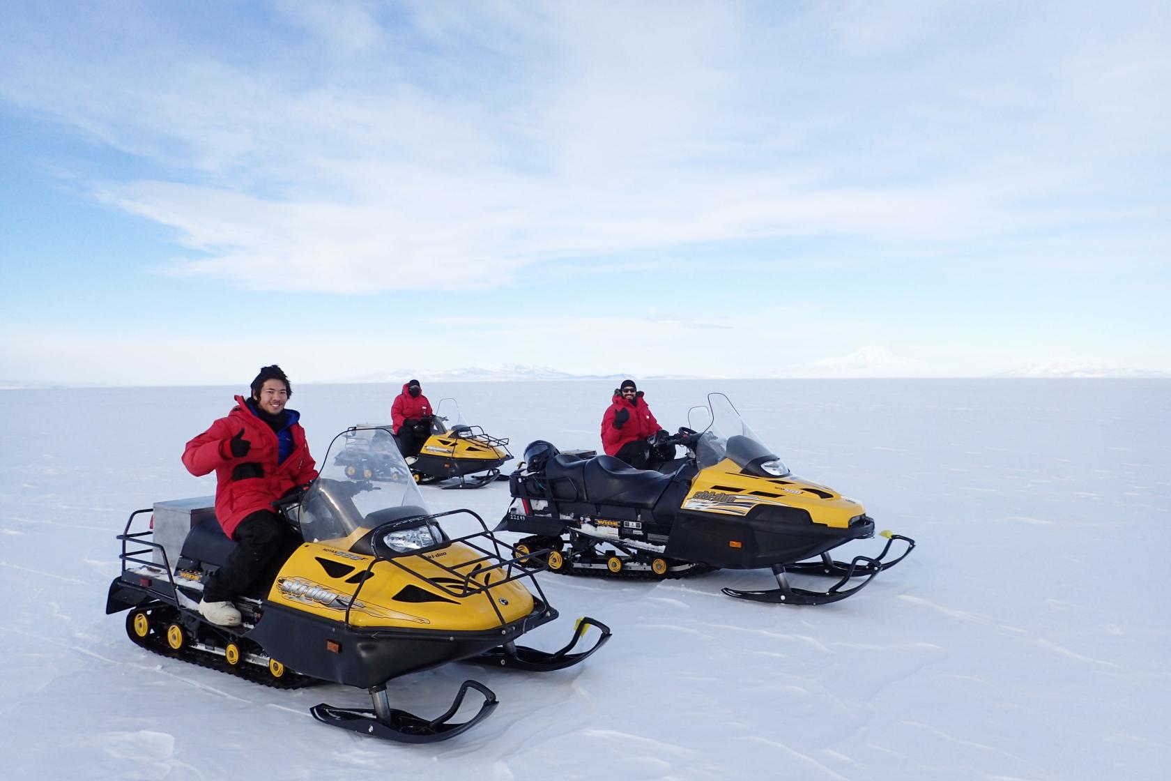 Three students of the Hofmann lab riding snowmobiles in Antarctica