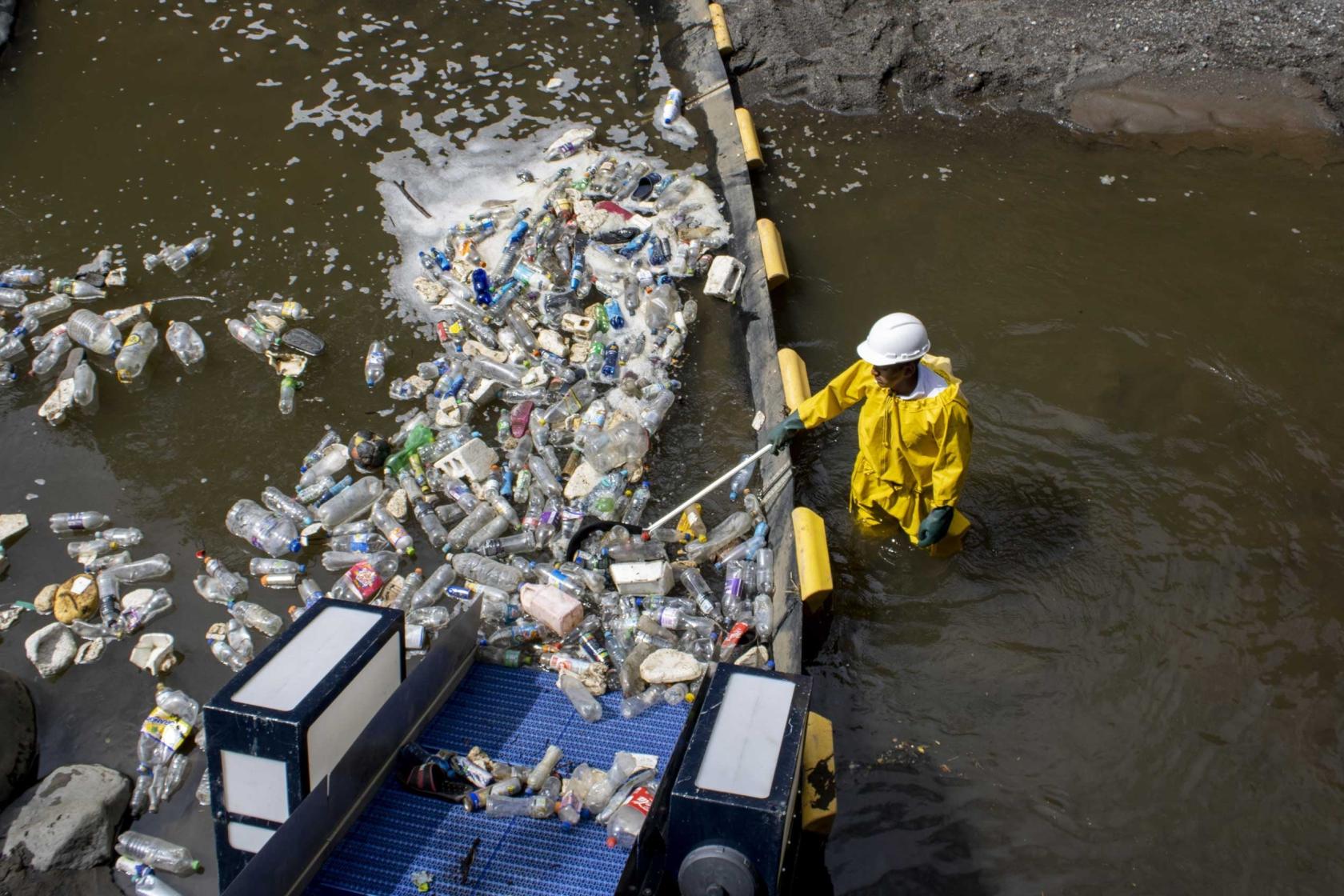 Man in yellow coat is removing plastic from river water