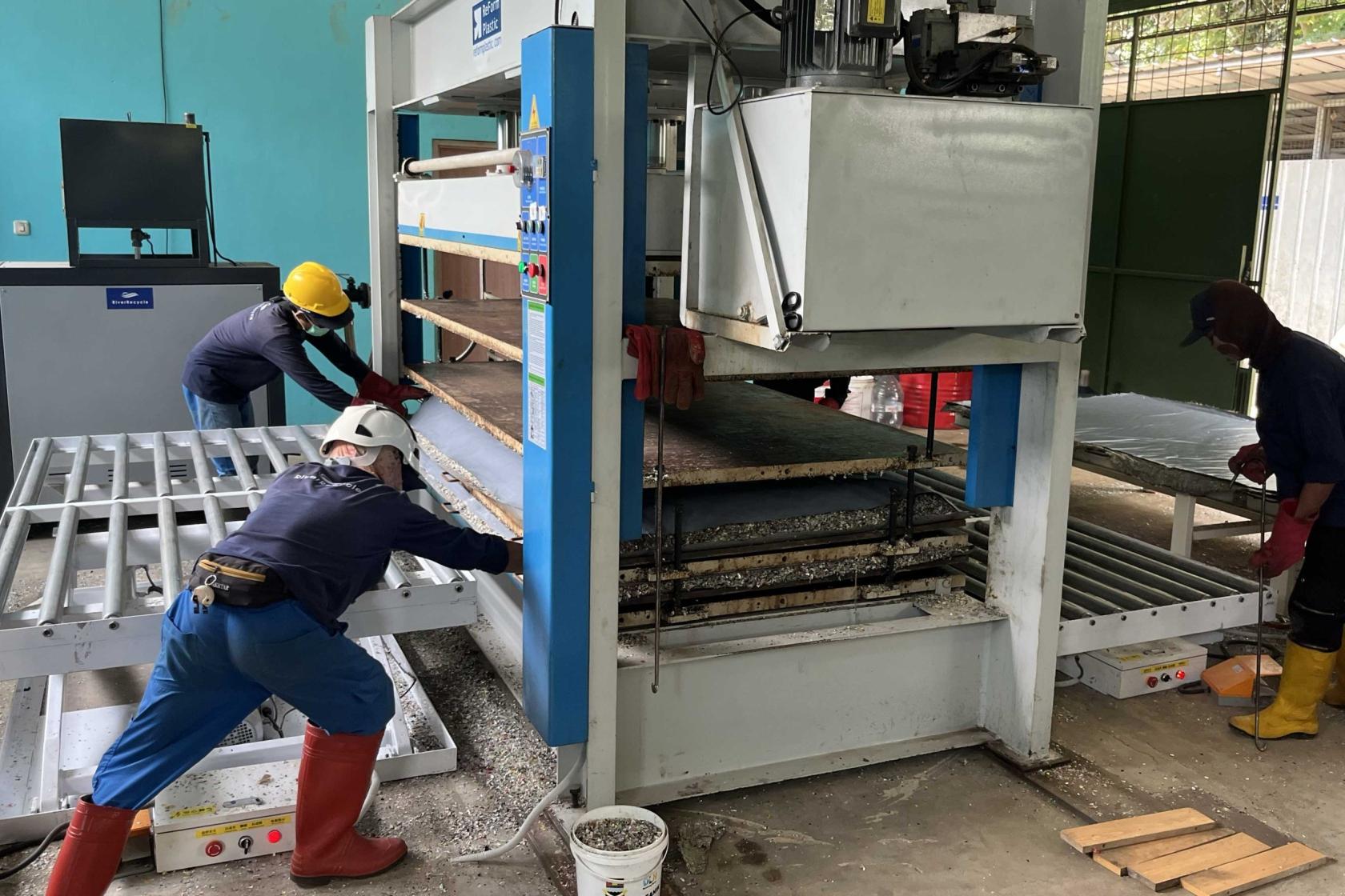 Crew operating machinery to turn plasic into plywood boards