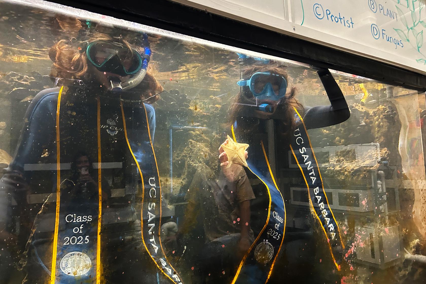 Marine (left), and Gainna (right) inside a REEF tank wearing their wetsuit, mask, and UCSB stole